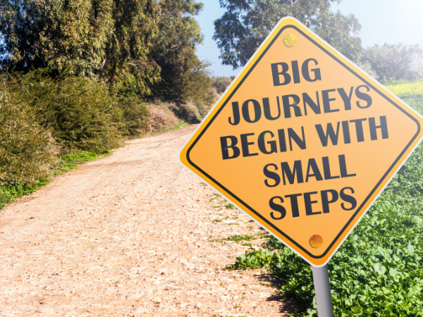 Sign on a winding path that says BIG JOURNEYS BEGIN WITH SMALL STEPS